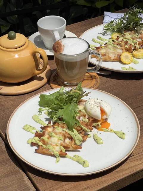 Waffles con huevo pochado y salsa verde, junto a un latte y la tetera amarilla