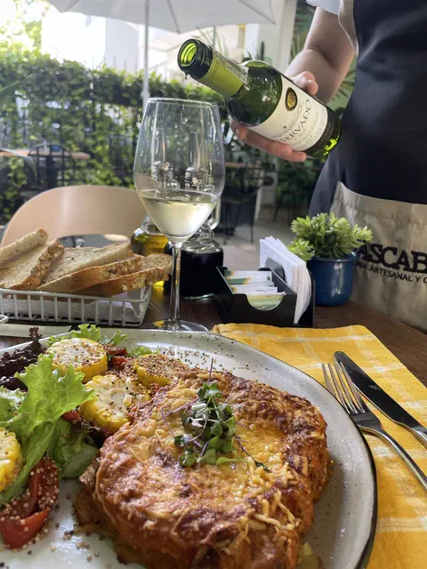 Un mesero sirve vino blanco en la terraza junto a un plato gratinado